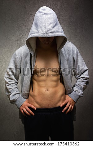 Muscular young Caucasian handsome man with hoodie after workout. Dark wall textured background.Fitness, bodybuilding and healthy lifestyle concept.