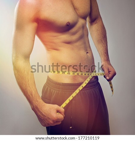 Closeup of fit young Caucasian man\'s torso. Man using tape measure. Fitness, diet, healthy lifestyle.