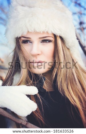 Beautiful young blonde Caucasian woman with white fur hat and gloves with bright makeup posing outdoors in winter. Beauty and makeup concept.