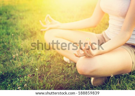 Young Caucasian fit and slim woman doing yoga outdoors in summer. Woman sitting in grass in yoga position with hands on her knees. Yoga lifestyle concept.