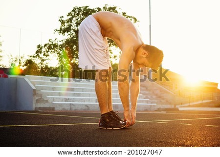 Handsome fit young Caucasian muscular man doing workout outdoors in summer stretching out. Golden hour shot. Natural lens flare effect.