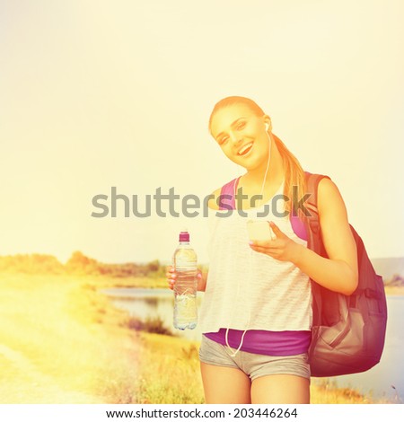 Beautiful young runner woman with smartphone,water and backpack outdoors on sunny summer day. Square image. Instant filter instagram look. Sunset at the lake after fitness workout.