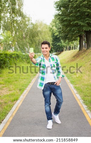 Handsome young mixed race hipster man taking a selfie in park. Full body portrait of teenage guy taking a self portrait outdoors.