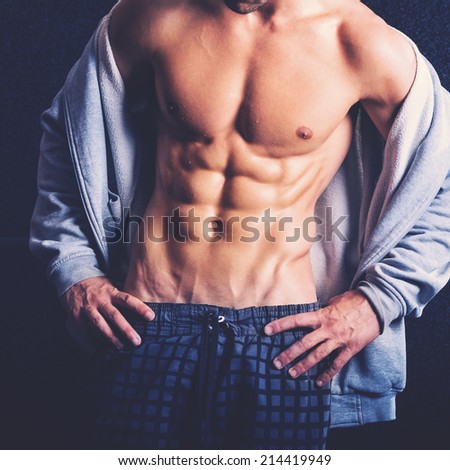 Handsome slim man with muscular body. Closeup of fit young man\'s abdomen against dark background. Color filter applied.