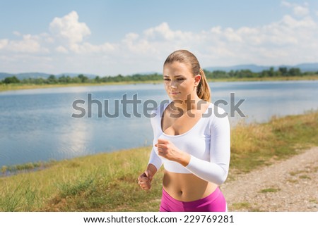 Cute fit young blonde Caucasian woman jogging outdoors in summer. Runner teenage girl in white and pink sportswear at the beach. No retouch.
