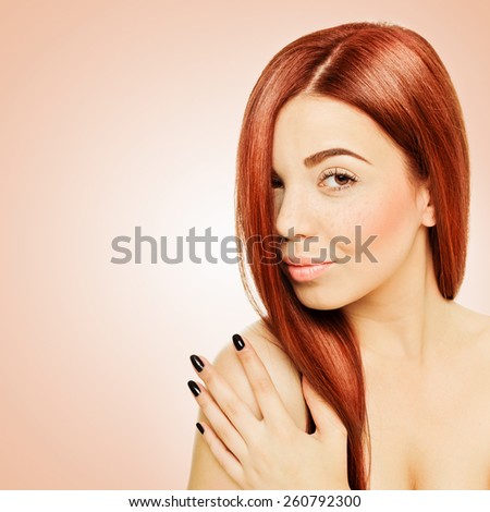 Closeup head shot of gorgeous redhead Caucasian young woman with freckles, pastel peach colored makeup and black manicure. Peach and white colored background, square format, retouched.