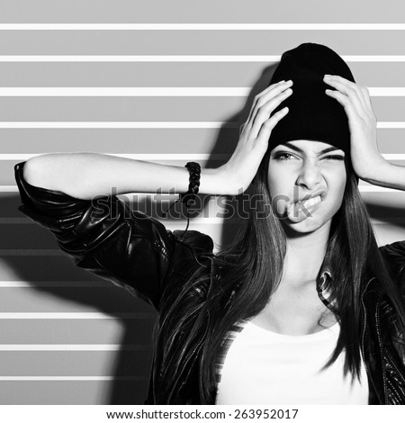 Beautiful hipster Caucasian brunette teenage girl with black beanie hat and black leather jacket posing making funny facial expression. Medium retouch, black and white, square format.