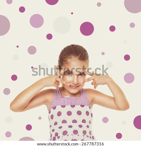 Happy little playful Caucasian girl in white dress with purple dots with hands in front of her face. Square format image, retouched, filter applied, beige background with random purple dots.
