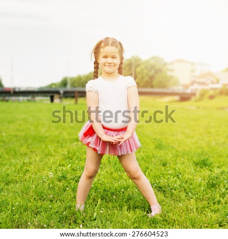 Cute happy little girl wearing tutu in park in summer. Beautiful five year old blonde girl with braids posing in park on sunny summer day. Retouched, natural light, square format.