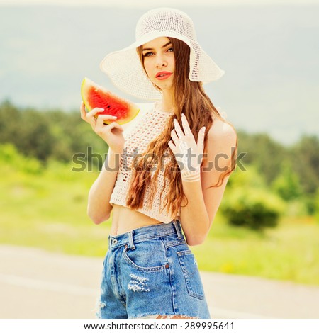 Fashionable young woman in crochet top, crochet hat and blue denim shorts outdoors on sunny summer day holding a slice of watermelon. Square format, retouched, vibrant colors.