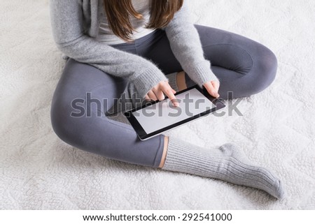 Closeup shot of unrecognizable young woman in gray loungewear and socks sitting in bed at home using digital tablet. Female wearing gray outfit at home. Horizontal, no retouch, natural light.