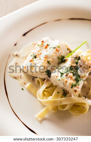 Cooked hake with sauce and pasta.