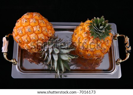 Two pineapples on the tray against black background
