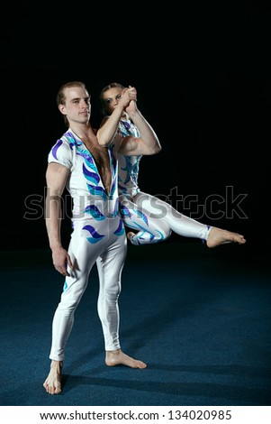 Circus artists perform different tricks. Man holding woman with his arm.