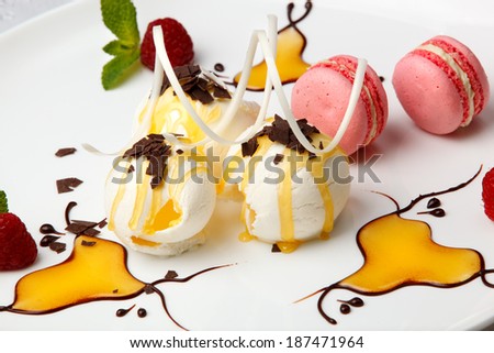 Pink macaroons with vanilla ice cream topped with golden honey or syrup and chocolate flakes with a decorative chocolate whirl and garnished with fresh berries