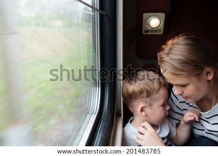 Loving attractive mother and her cute young son on a train trip sitting alongside the window in the compartment as she adjust his clothing