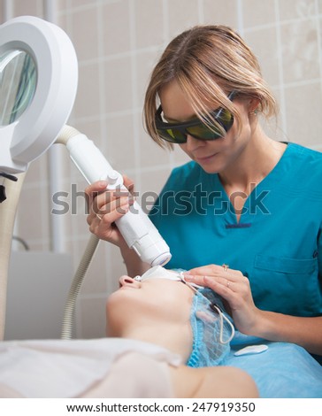 Cosmetician in safety glasses using laser for facial treatment in cosmetology clinic