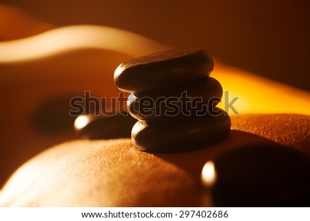 Close-up shot of woman receiving hot stone massage at beauty spa. Black rocks on the skin shining in sunlight