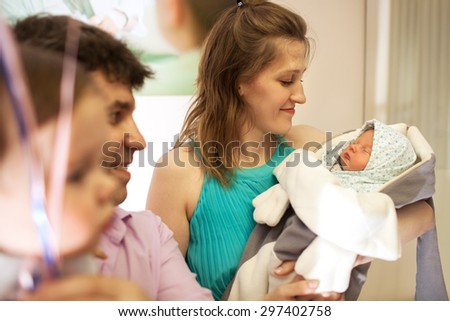 Side view of a happy family in the maternity hospital, father holds elder son, mother stands with infant