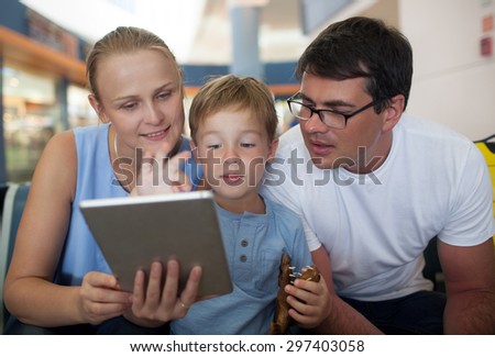 Young parents and little son at the airport. Mother holding pad and boy playing game, both parents looking at screen. Entertaining during flight waiting