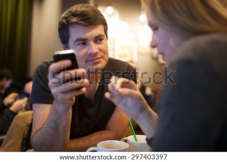 Young man using cellphone during the meeting with a girl in a cafe, but his look is attracted by someone else