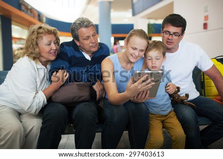Happy big family at the airport. Child, parents and grandparents  watching something on tablet computer to fill in time while waiting in the lounge