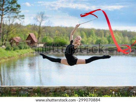Young rhythmic gymnast doing split jump during ribbon exercises.