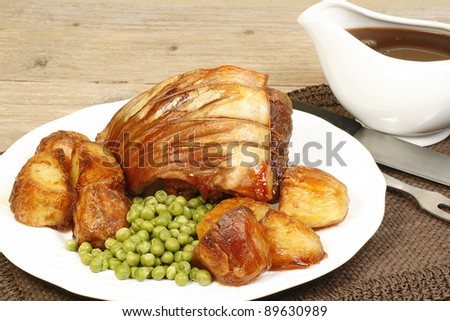 roast pork shoulder joint with roast potatos peas and gravy