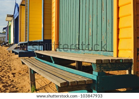 Old paint on stairs in bright sunlight on sandy beach with row of colorful swim cabins in Victoria, Australia
