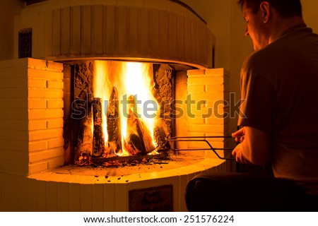 Man adjusting firewood in burning fireplace