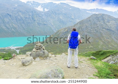 Back of a man with blue backpack in mountains looking away