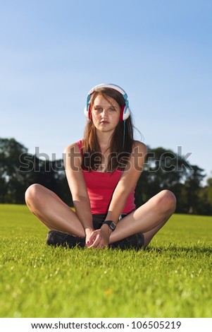 Young girl with headphone in the park with relaxed face expression listening music and exercising