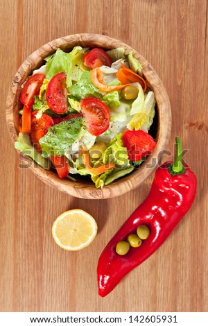 Bowl made of olive wood filled with cos and iceberg lettuce salad with paprika, carrots, tomatoes and green olives on wooden table. More healthy food in my portfolio