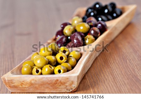 Variety of green, black and mixed marinated olives in olive tree dish on wooden table. Selective focus