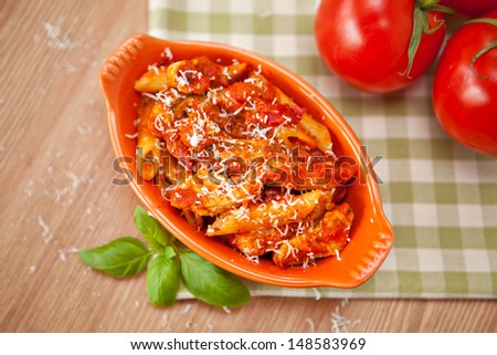 Individual casserole dish with spicy penne pasta on checkered green cloth. Shallow depth of field