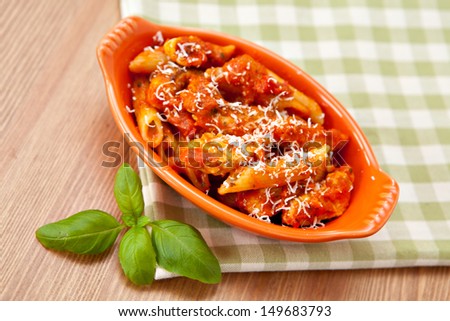 Individual casserole dish with spicy penne pasta on checkered green cloth. Shallow depth of field