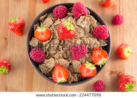 Bran flakes with fresh raspberries and strawberries on wooden table. Healthy eating choice concept