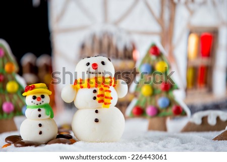 Decorative snowmen and gingerbread house with lights inside on black background. Rural Christmas night scene