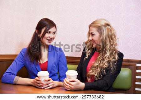Two young pretty caucasian girls with long hair drinking coffee, chatting and having fun at a cafe