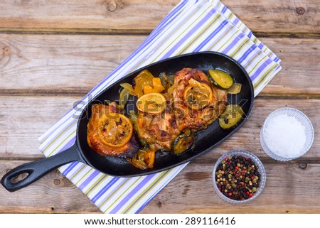 Delicious baked chicken thighs with lemon slices, onion and zucchini served in cast-iron frying pan on rustic wooden table