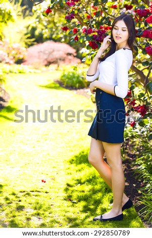 Young beautiful tall woman with long straight dark hair posing at spring garden