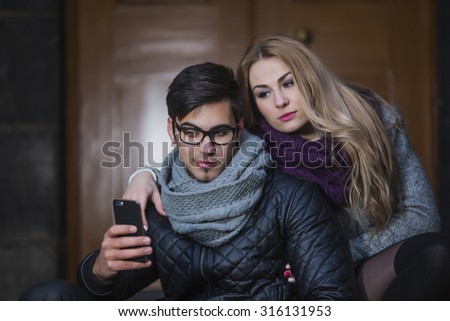 Young man and woman on stairs of old building making selfie and looking at the smart phone