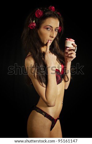 Young woman in red lingerie eating cake. Isolated on black. Low key