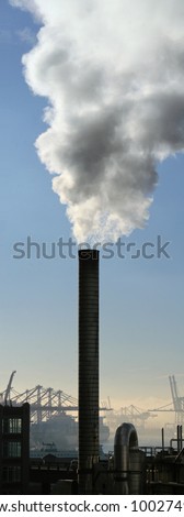 Large smoke stack spewing steam with shipping port cranes in the background and blue sky above./ Port of Seattle Smoke Stack /  Industrial output.