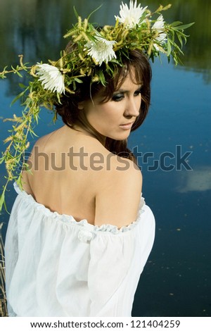 alluring wood nymph standing with her back near the lake. beautiful dark haired woman with a wreath on her head on the background of the lake