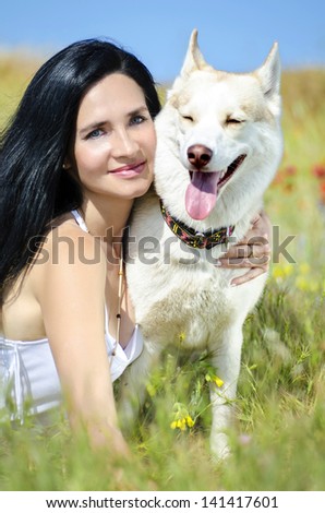 Beautiful woman with husky outdoors.Happy brunette woman with smiling siberian husky dog, sitting in a flowering field on a sunny day, on a walk with dog