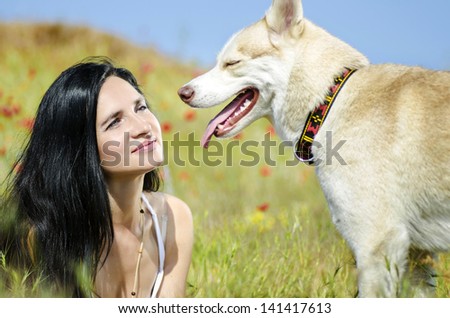 Beautiful woman looking at husky outdoors.Happy brunette woman with smiling siberian husky dog, sitting in a flowering field on a sunny day, on a walk with dog