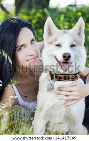 Romantic young woman and white husky outdoors.Happy brunette woman with smiling siberian husky dog, sitting in green forest in shadow, on a walk with dog