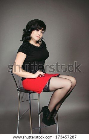 Beautiful fashionable woman in studio. Fashion portrait of young sexy alluring woman girl in red skirt and black stockings posing on gray background. Sex-bomb.