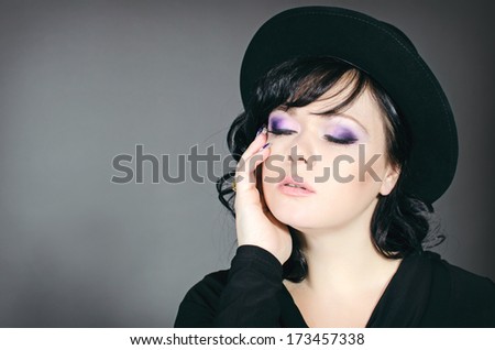 Beautiful brunette woman in stylish black hat posing in studio. Romantic lady in black on gray background. Fashion portrait.